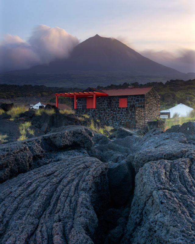 ancient volcanic rock below a house made from volcanic rock. Volcano behind it.